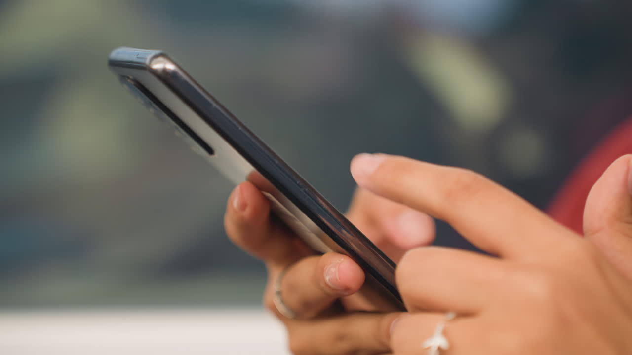 Persona che usa il telefono in treno. Un passeggero si concentra sul dispositivo mentre è seduto nel vagone del treno. Un individuo che digita messaggi e scorre la chat sul telefono durante il viaggio in treno, con il cavo degli auricolari visibile.