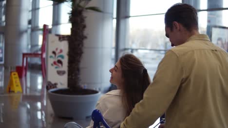 Funny-couple-in-airport.-Attractive-young-woman-and-handsome-man-with-suitcases-are-ready-for-traveling.-Having-fun-on-luggage