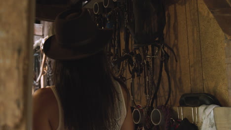 cowgirl searches for her horse riding gear on the wall of a rustic old barn