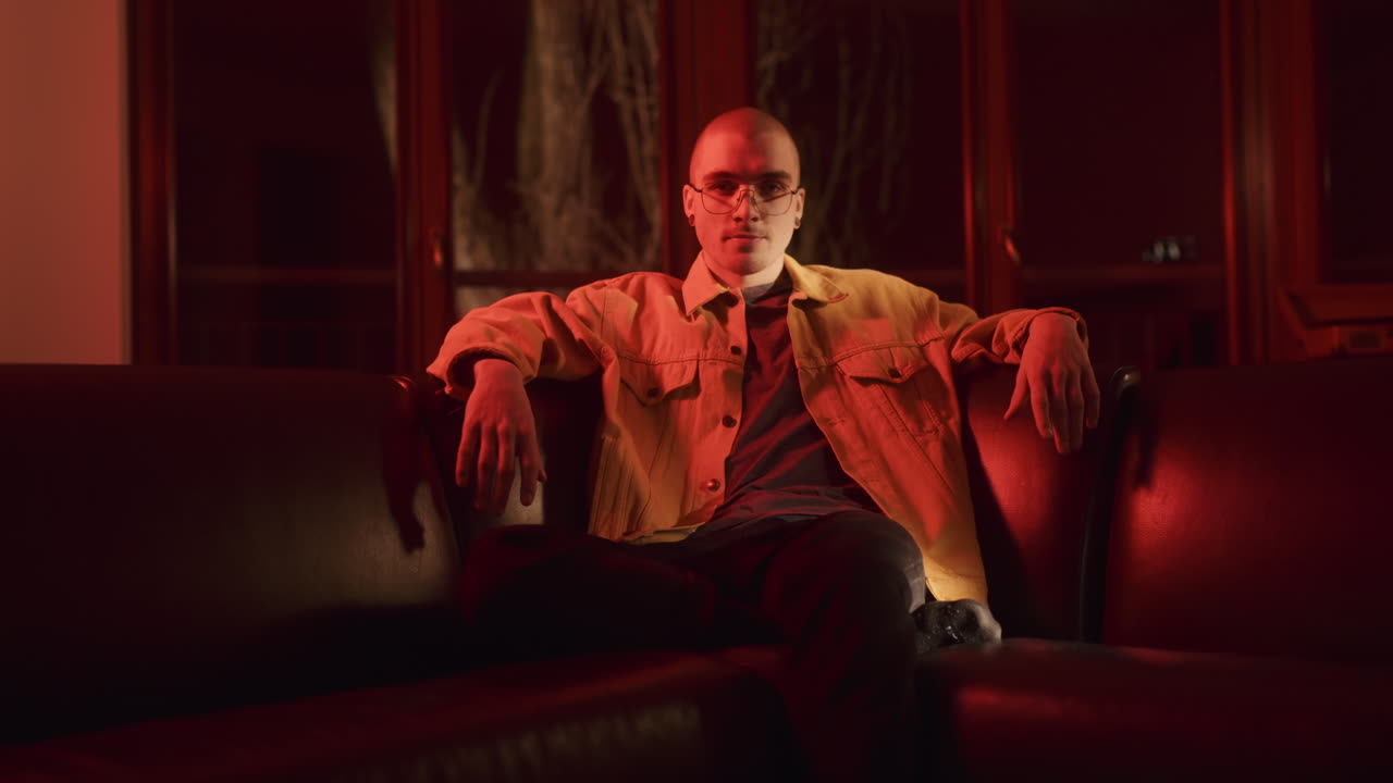 Man in Yellow Jacket Sitting on a Couch Under Red Light
