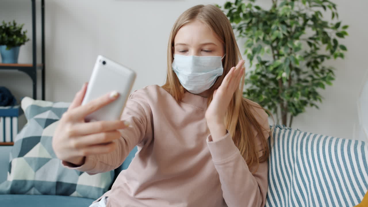 Teenage girl taking a selfie while wearing a face mask at home.