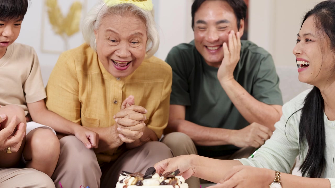 暖かい家庭で、アジア人家族がケーキ、ろうそく、笑い声とともに祖母の誕生日を祝う。