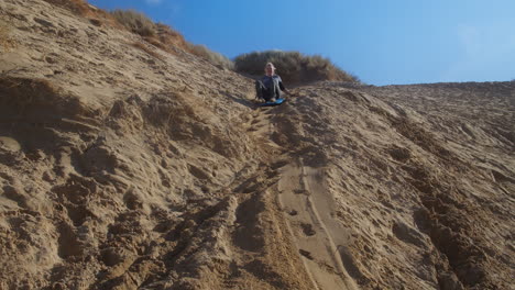 happy girl slides down sand dune on a blue sledge