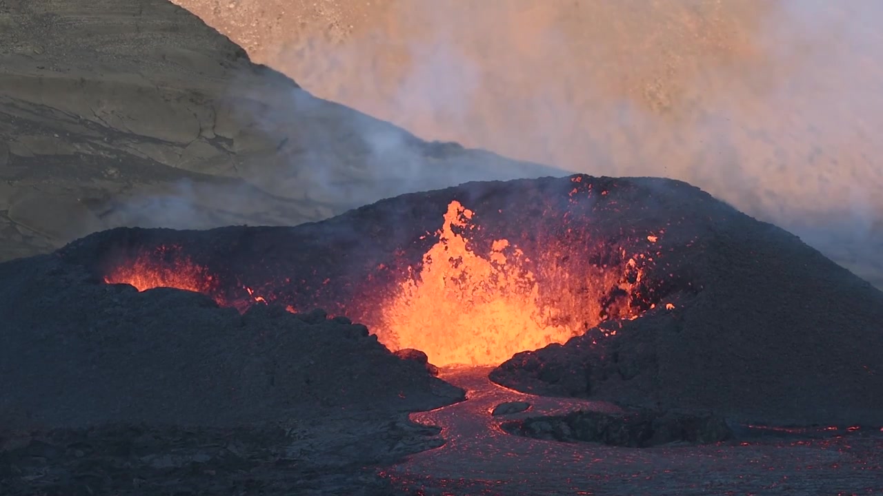 Vista aerea con drone al rallentatore di un'eruzione vulcanica attiva in Islanda che mostra lava fusa brillante che sgorga da una bocca vulcanica e scorre su basalto scuro con vapore che sale
