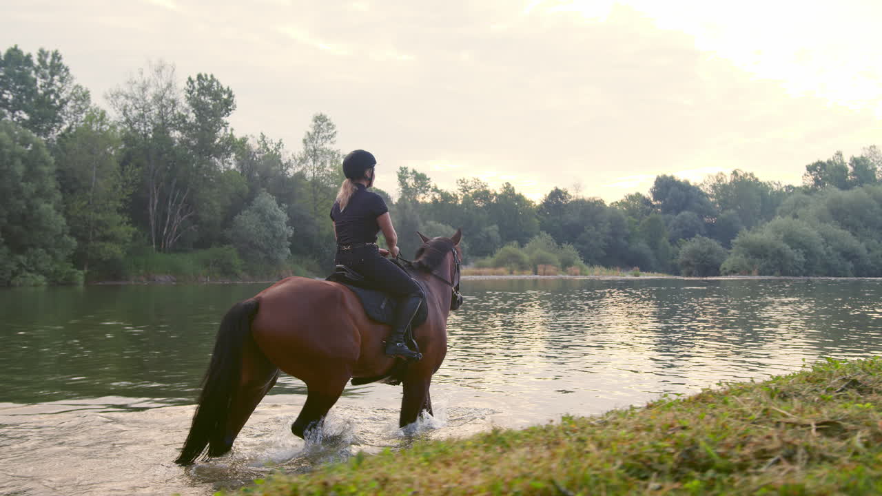 mujer a caballo montando un caballo a lo largo del río al atardecer, vista lateral