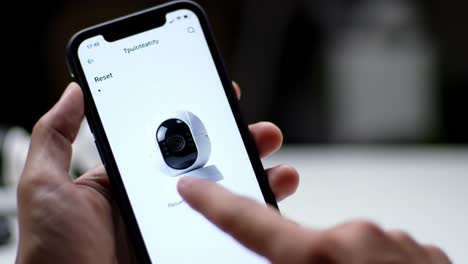 a person interacts with a smartphone app to adjust settings on a security camera. the focus is on home security while exploring camera features in a relaxed night setting.