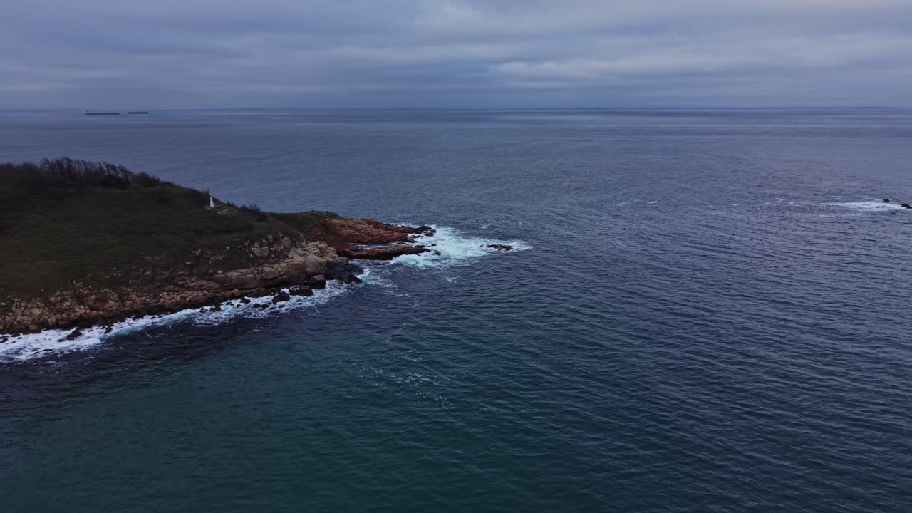 Vista di una costa rocciosa e mare calmo sotto un cielo nuvoloso al crepuscolo