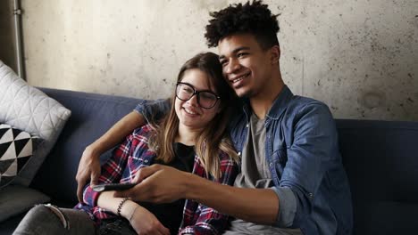 cute happy couple of young hipsters smiling and cuddling on the couch while trying to find a perfect tv channel. leisure time, enjoying youth, living together. relationship goals.