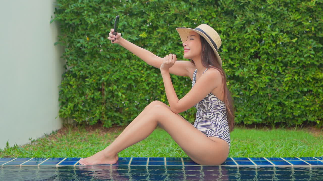Woman in swimsuit sitting on edge of swimming pool takes a selfie