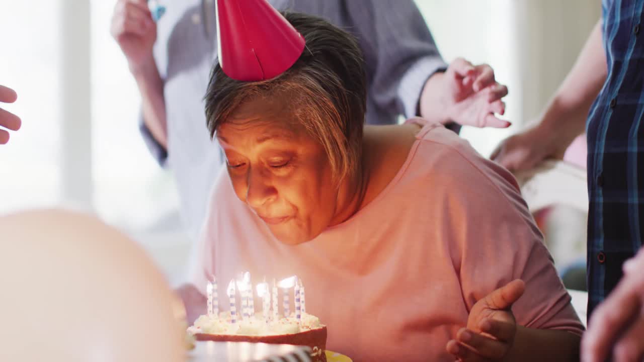 Uomo anziano caucasico e felice a una festa di compleanno con torta, insieme ad amici anziani di diverse etnie, al rallentatore.