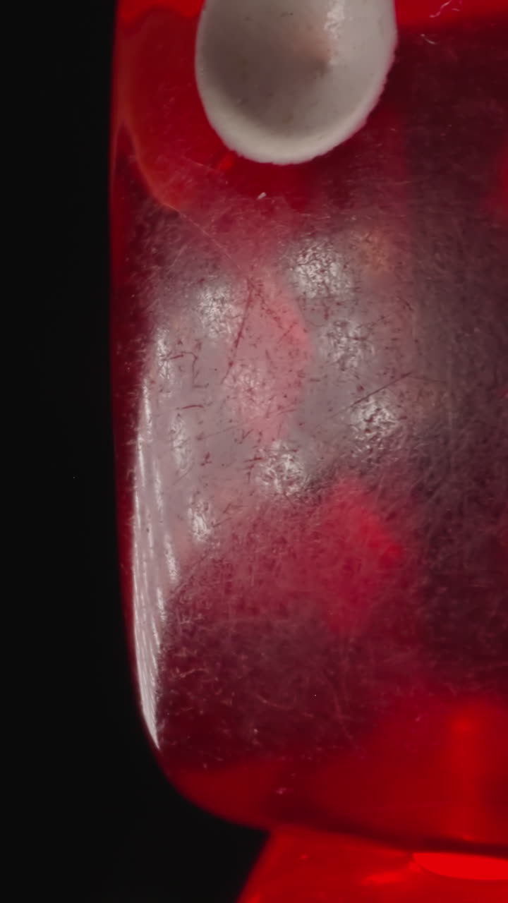 Transparent red dice with white dots reflecting bright studio light spins. Small cubes created for playing gambling games on black background macro