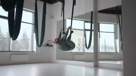 young smiling woman practice in aero stretching swing. aerial flying yoga exercises practice in green hammock in fitness club