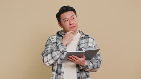 Asian man making notes writing thoughts with pen into notepad notebook diary to do list good idea