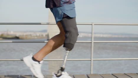 primer plano de un deportista irreconocible con una pierna artificial corriendo a lo largo del terraplén por la mañana