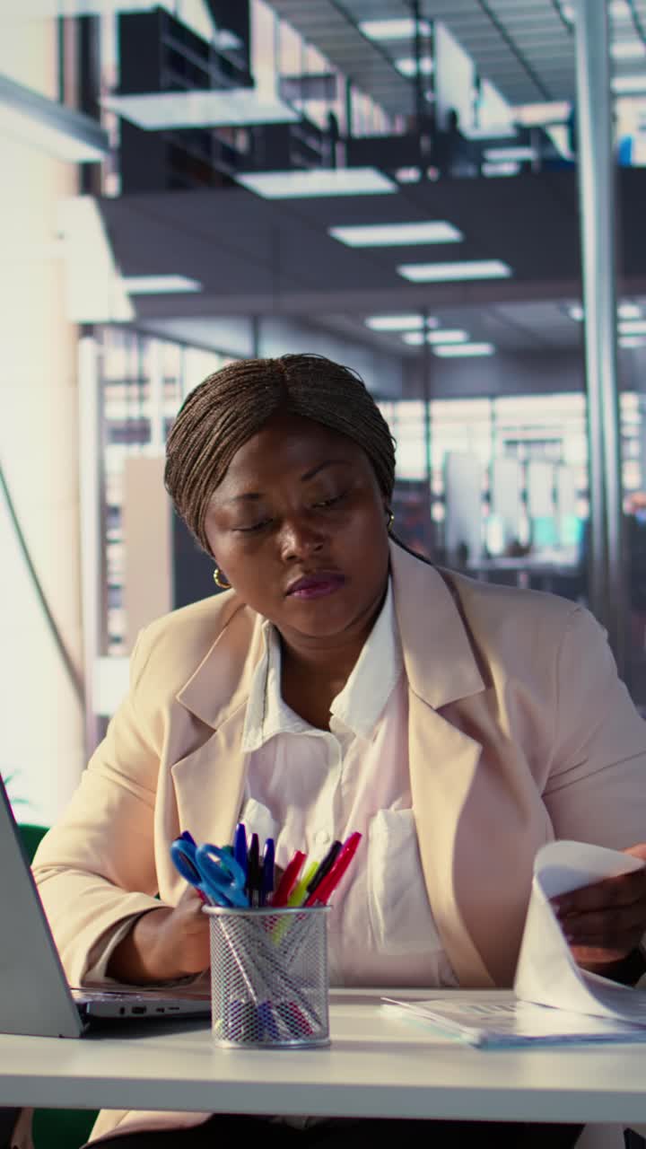 Empresária afro-americana trabalhando em laptop e documentos no escritório.