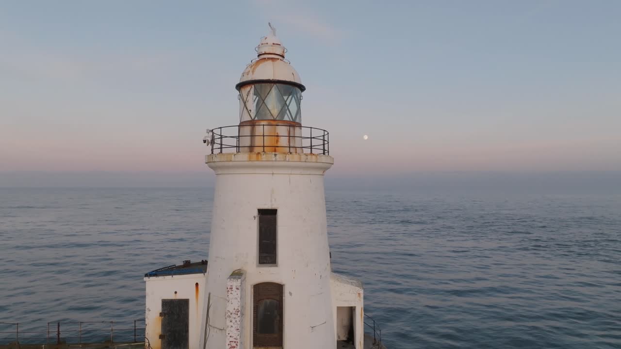 Rustic lighthouse with calm ocean and pastel skies at sunset