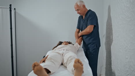 therapist doing manual treatment in clinic ward. grey hair osteopath bending