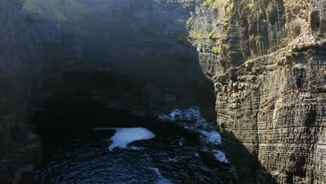 panoramic aerial shot at the mouth of a cliff inlet, revealing intricate cliff layers and textures, with sunlight highlighting the natural formations