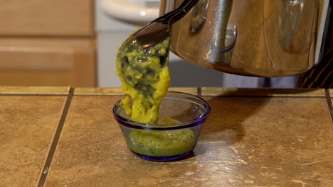 sirviendo una cucharada de queso nacho vegano en un tazón de vidrio pequeño, cerrado