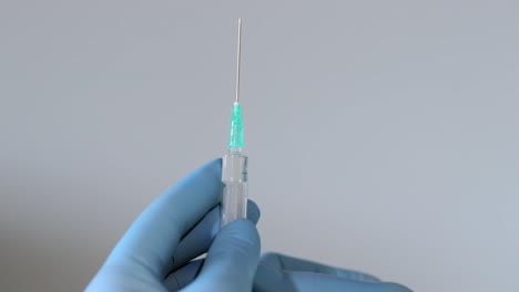 extreme close up shot of doctor's hands wearing surgical gloves and squirting air from syringe through a sharp needle on a isolated background