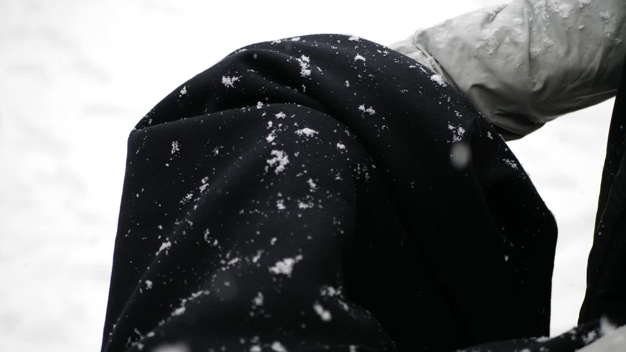 Fluffy snow flakes falling on a black jacket during a winter weather storm SLOW MOTION