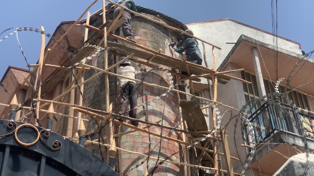 behind the fence, workers are chiseling old stones to renew them