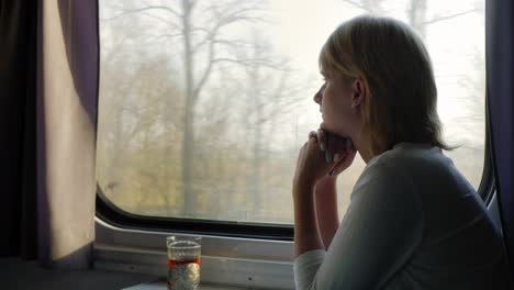 a comfortable trip a young woman is traveling on a train beside her there is a cup of tea in a cup h