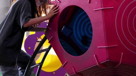 a young person climbs a colorful indoor playground structure, ascending a ladder toward a tunnel under bright, even lighting. camera follows with steady, medium-close shots