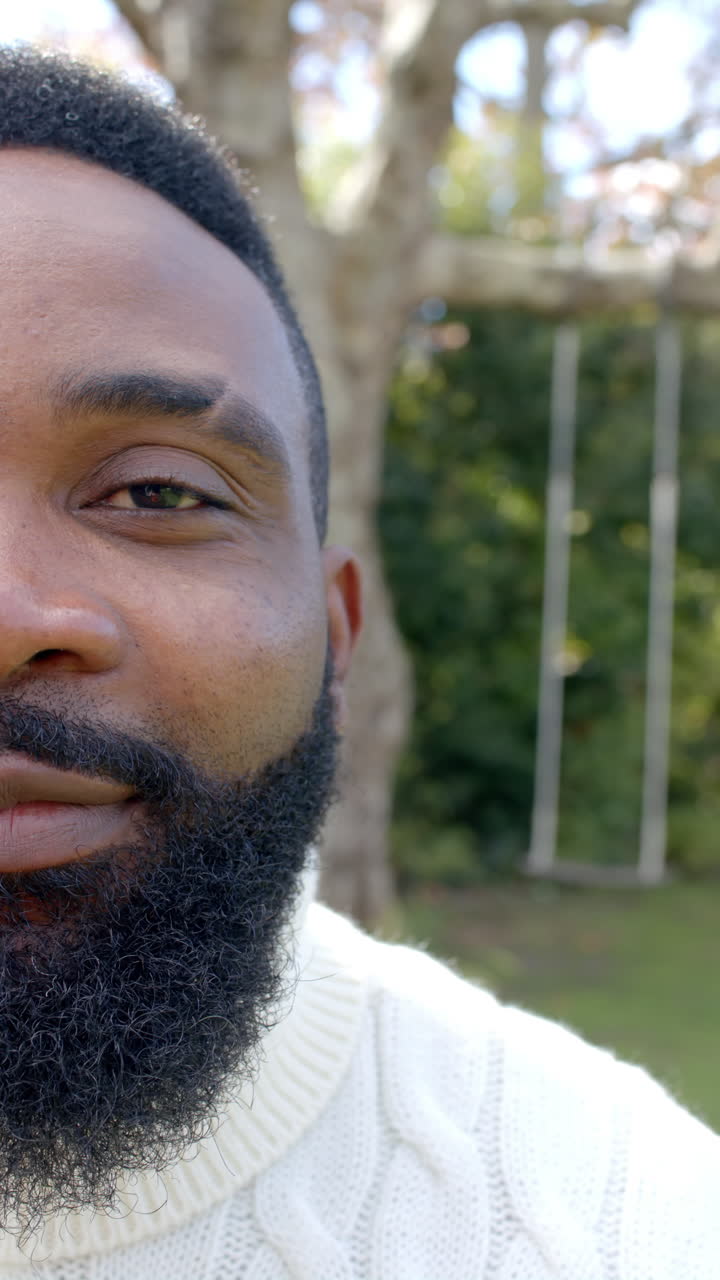Vertical video of half portrait of african american man in sunny garden, slow motion