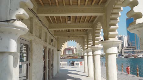 revealing shot of a woman walking on promenade by waterfront building with arabesque arches in al fahidi neighborhood - tilt-down