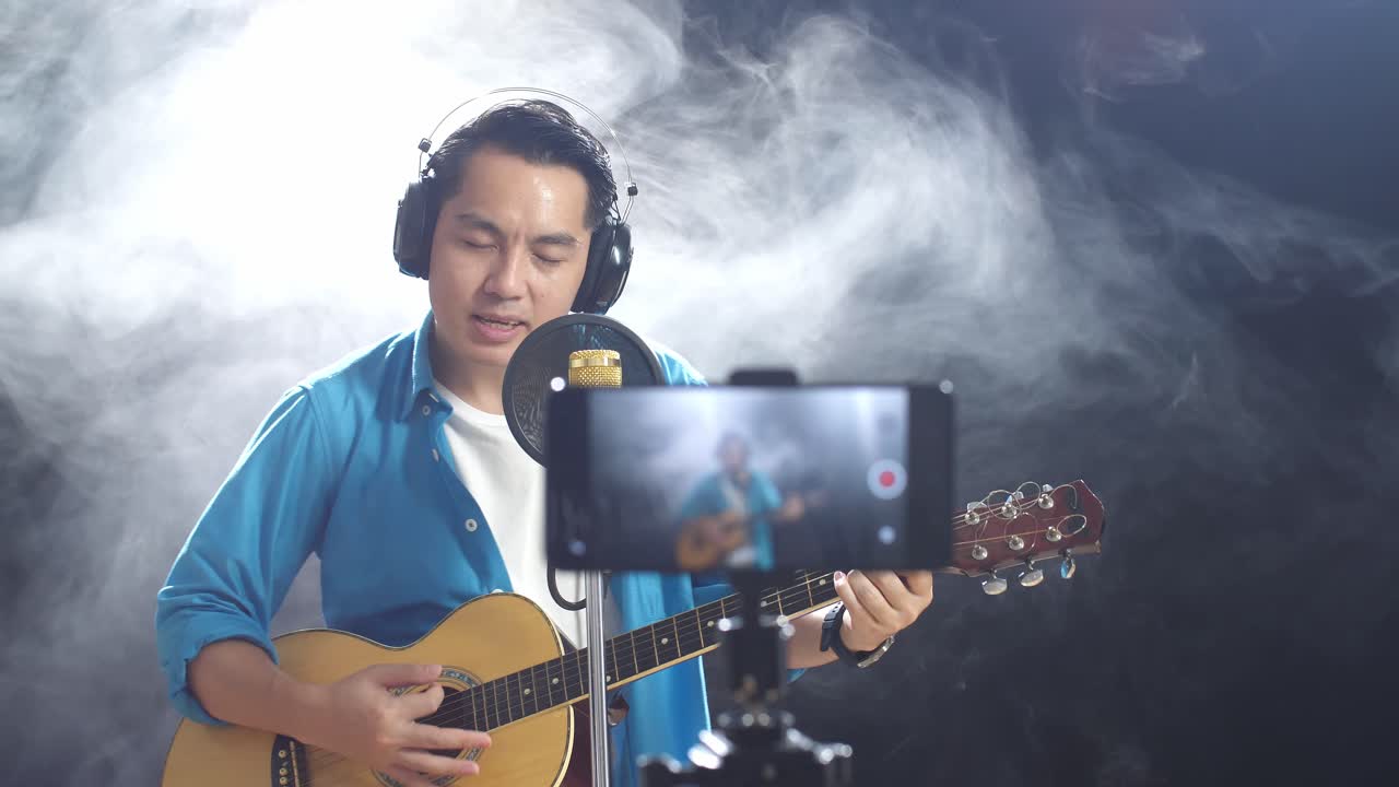 비디오 를 녹음 하는 동안 남자 가 노래 하고 어쿠스틱 기타 를 연주 하고 있다