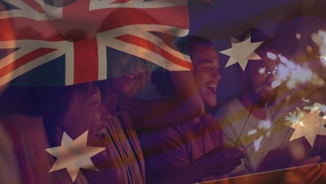 composite video of australia flag over group of diverse friends celebrating with sparklers at beach