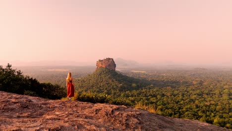 a woman calmly walks across the summit of pidurangala rock, making her way to witness the breathtaking sunrise over sigiriya rock.