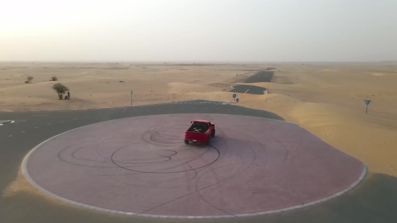 el camión rojo hace un donut en medio de una rotonda de la carretera del desierto al atardecer antes de alejarse a toda velocidad por la carretera