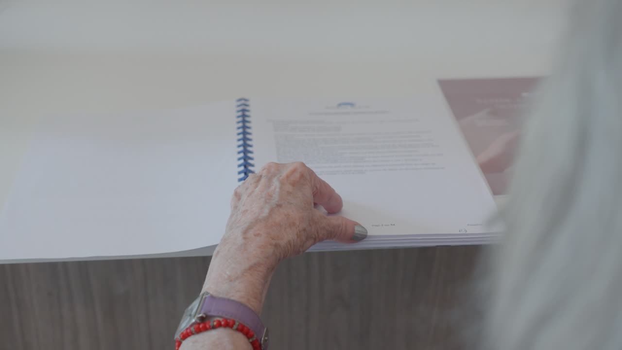 sobre el hombro de una mujer anciana volviendo las páginas de un libro