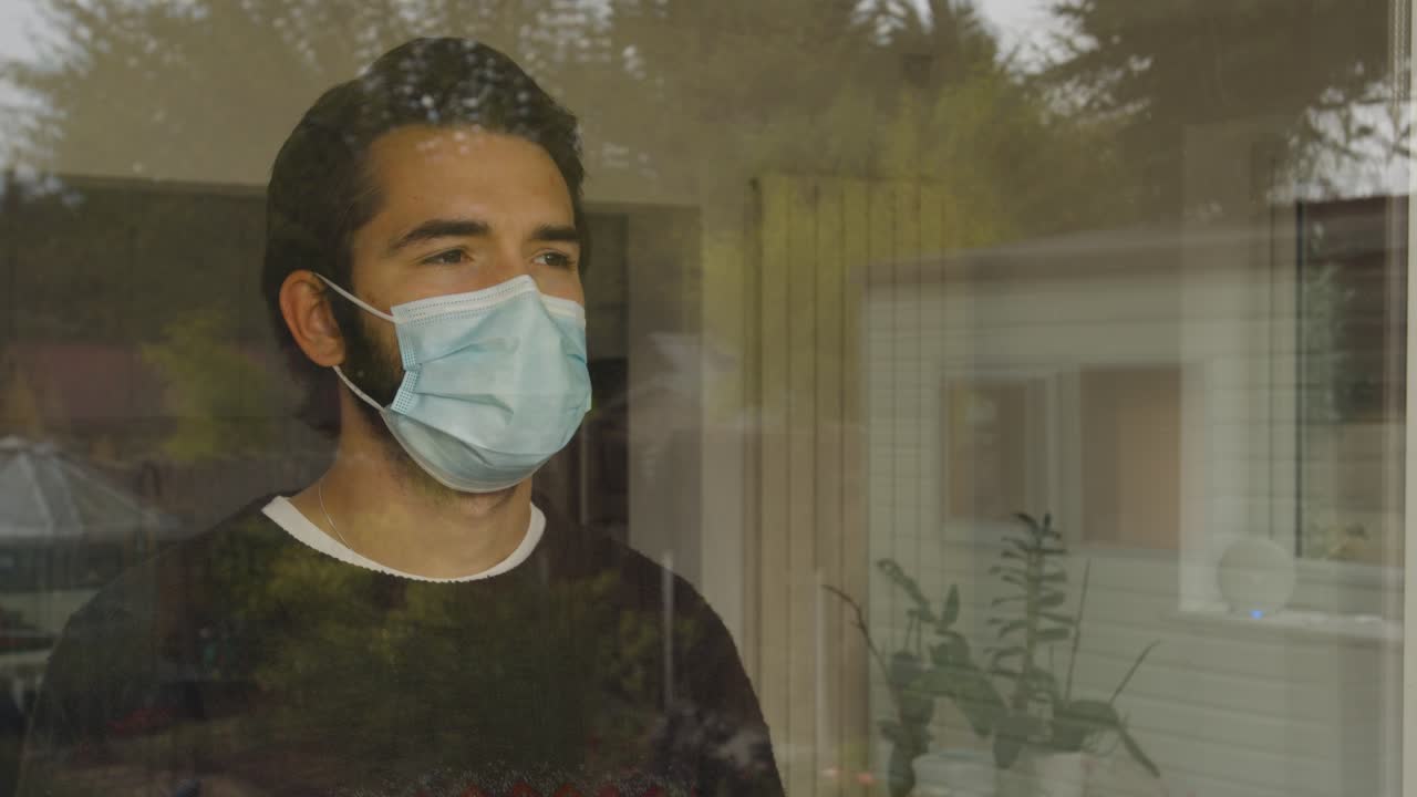 Male looking out of a window wearing a facemask in quarantine