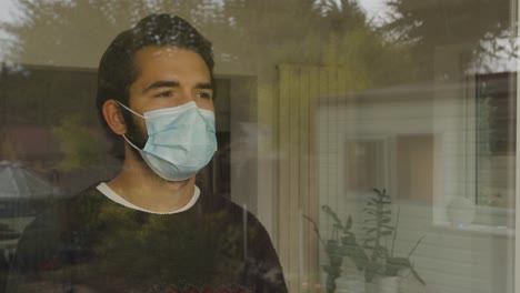 Male-looking-out-of-a-window-wearing-a-facemask-in-quarantine