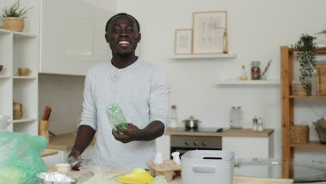 portrait of cheerful black man sorting plastics at home