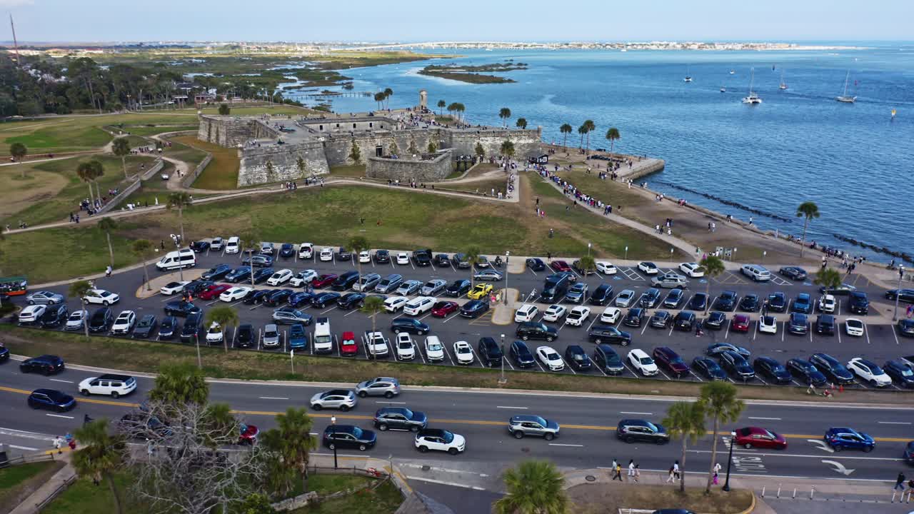 Lo storico forte Castillo de San Marcos si affaccia su un lungomare ricco di auto, visitatori, palme e calme acque blu con barche ancorate al largo a St. Augustine.