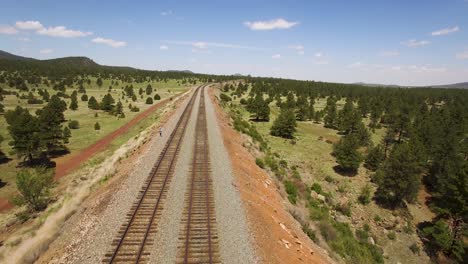 aerial pull away from a single man standing along the parallel train tracks​ near williams, arizona