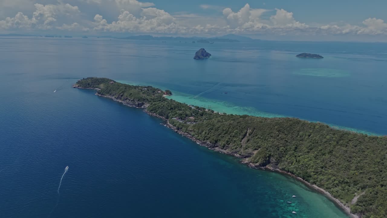 Drone slowly pans left across calm turquoise waters and dense tropical forest on a bright day in Phi Phi Islands, Thailand.