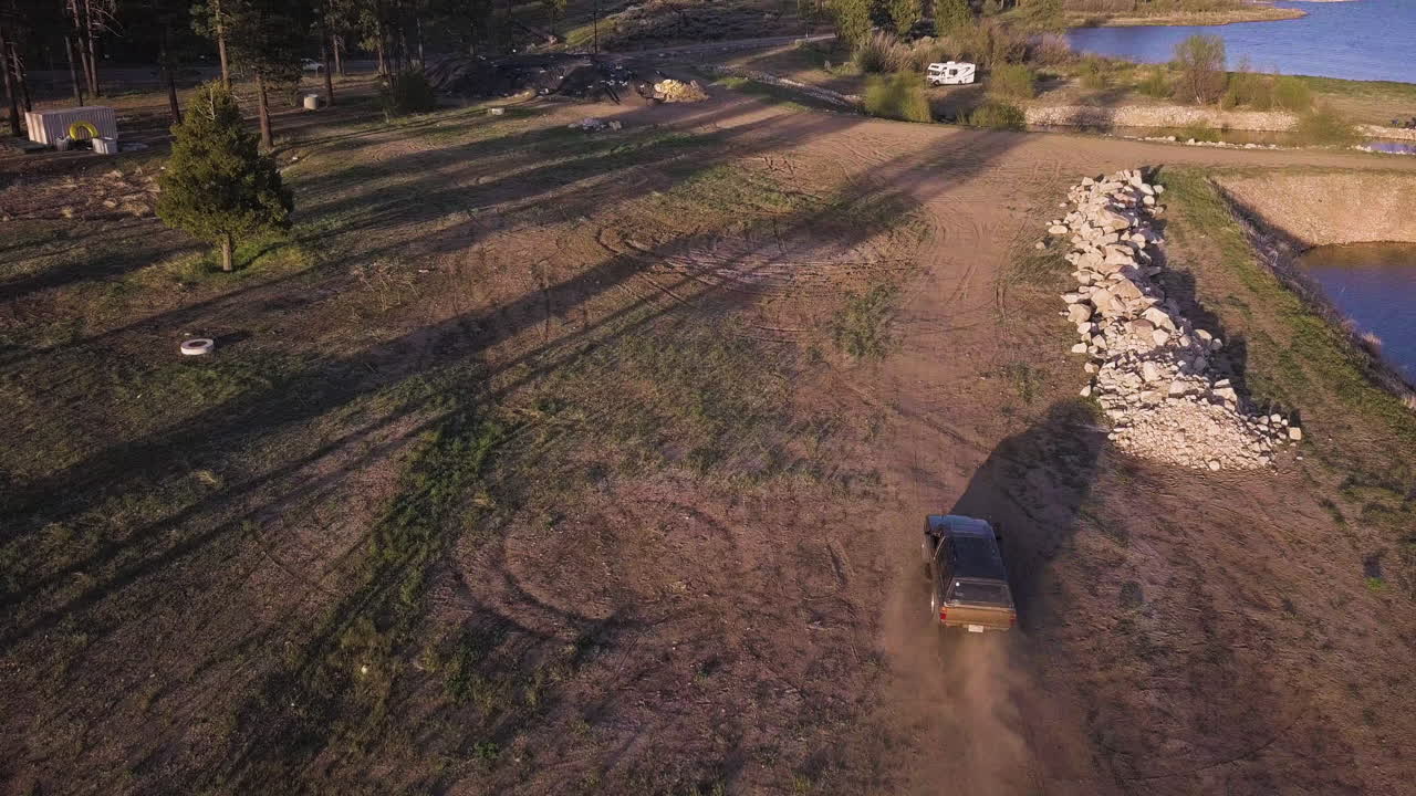 Black vehicle driving on dirt road on shore of big bear lake, California, aerial