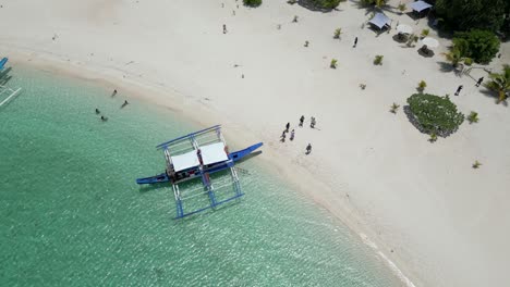 Top-down-aerial-descending-over-banca-boat-and-tourists-roaming-beach