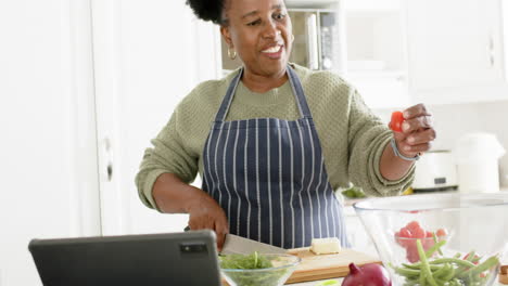 happy african american senior woman chopping vegetables and dancing in sunny kitchen, slow motion