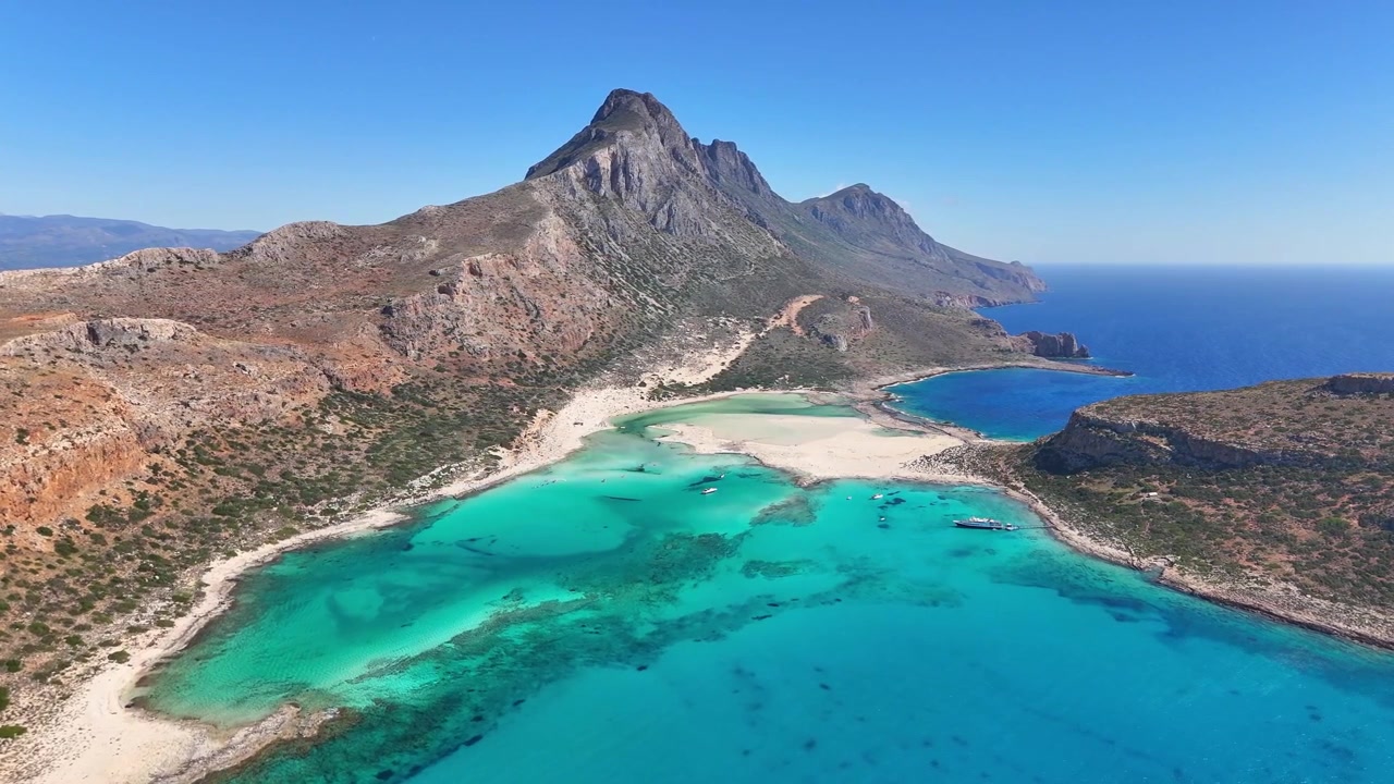 A Lagoa de Balos apresenta águas rasas turquesa e um banco de areia claro sob a Península de Gramvousa e uma crista montanhosa acidentada no oeste de Creta, paralaxe de drone