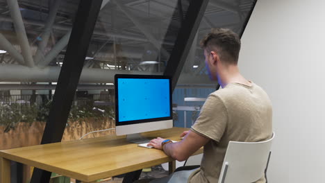 joven que trabaja en una oficina moderna en una computadora moderna, código de vestimenta informal