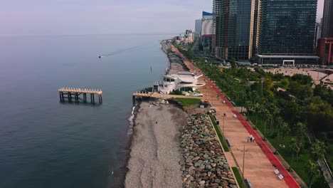 black sea beach alongside city promenade with modern apartment buildings and skyscrapers