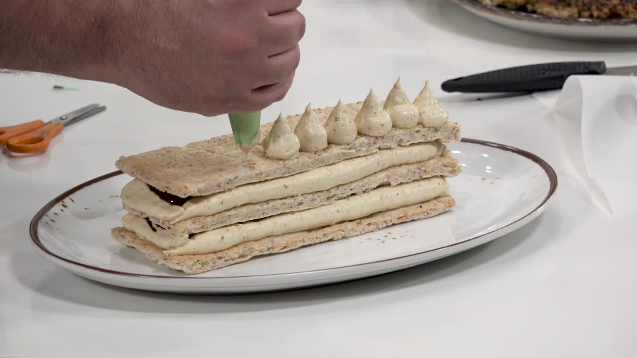 In a culinary workshop, an expert demonstrates the art of crafting a layered dessert using crisp pastry and creamy filling. Participants observe the intricate techniques involved in dessert making