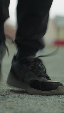 close-up of a person s legs jogging in an increasing pace, in black jeans and black sneakers, with a blurred background that includes a bench and a painted yellow building