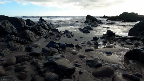 ocean water crashing onto beach with rocks during low tide on sunny day